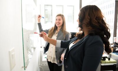 Two professional women discussing ideas on a whiteboard in a modern office setting.